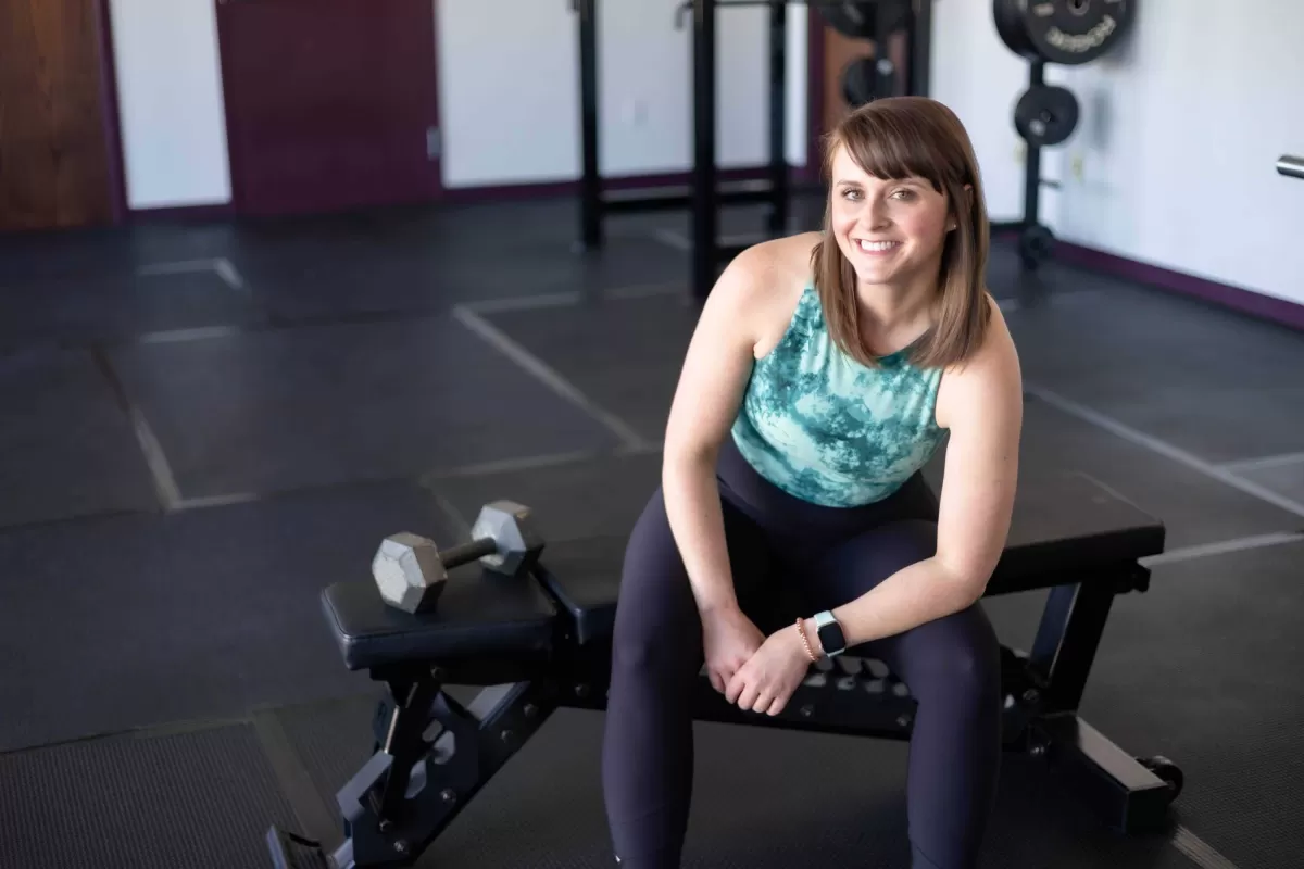 Alexis Reddig smiling while posing seated next to a dumbbell at simple solutions fitness