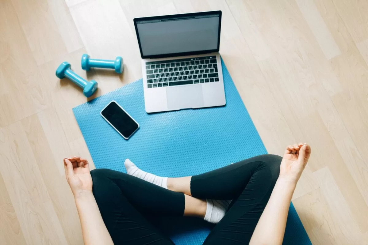 woman sitting on a yoga mat with light blue dumbbells laptop and smart phone
